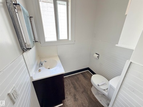 White tile wainscoting and beadboard paneling, wood-finish flooring, white vanity with integrated sink, and dual-pane window - 10416 100 Avenue, Westlock, AB - Indoor Photo Showing Bathroom