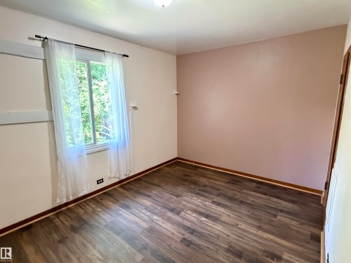 Wood-finish flooring, white trim, and a window with a dark rod - 10416 100 Avenue, Westlock, AB - Indoor Photo Showing Other Room