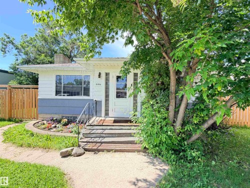 White siding exterior with a blue foundation, wood fencing, and mature trees - 10416 100 Avenue, Westlock, AB - Outdoor