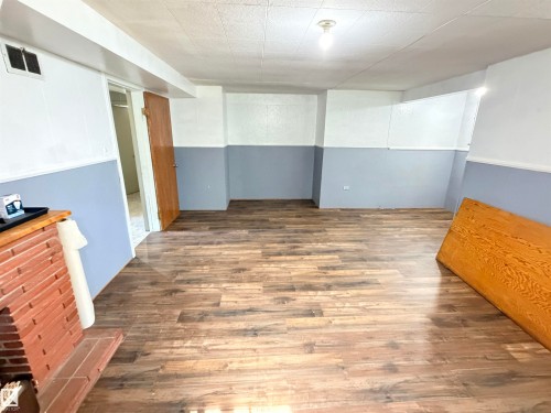 Spacious finished basement featuring wood-finish flooring throughout, two-tone wall treatment with crisp white upper walls and soft blue lower section, recessed ceiling lighting, and brick fireplace accent - 10416 100 Avenue, Westlock, AB - Indoor Photo Showing Other Room