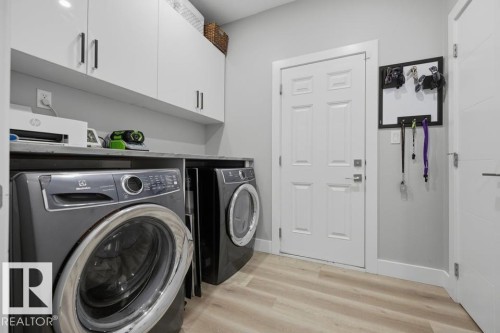 Laundry room featuring upper cabinetry with dark hardware, a dark countertop, light wood-finish flooring, and white paneled doors - 3303 Soleil Boulevard, Beaumont, AB - Indoor Photo Showing Laundry Room