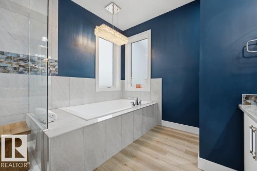 Soaking tub with dual windows, wood-finish flooring, and a crystal chandelier - 3303 Soleil Boulevard, Beaumont, AB - Indoor Photo Showing Bathroom