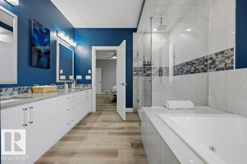 Dual vanity with undermount sinks, wood-finish flooring, built-in soaking tub, glass-enclosed shower, and tiled walls - 3303 Soleil Boulevard, Beaumont, AB - Indoor Photo Showing Bathroom