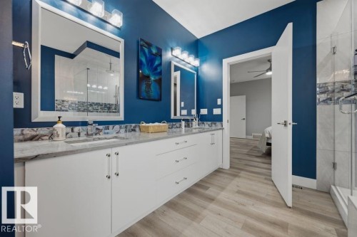 Dual vanity with undermount sinks, stone-finish countertops, extensive white cabinetry, wood-finish flooring, and a glass-enclosed shower - 3303 Soleil Boulevard, Beaumont, AB - Indoor Photo Showing Bathroom