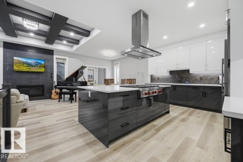Open-concept living space featuring a gourmet kitchen island with a built-in range, a stainless steel range hood, and light wood-finish flooring - 3303 Soleil Boulevard, Beaumont, AB - Indoor Photo Showing Kitchen With Upgraded Kitchen