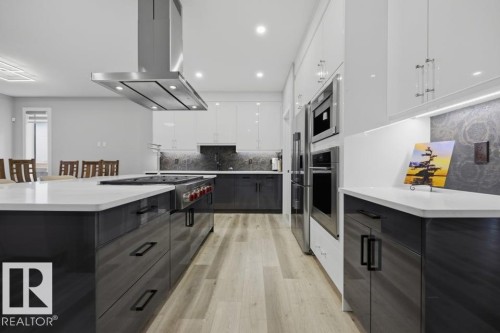 Gourmet kitchen featuring a large central island, stainless steel range hood, integrated oven, built-in refrigerator, and wood-finish flooring - 3303 Soleil Boulevard, Beaumont, AB - Indoor Photo Showing Kitchen With Upgraded Kitchen
