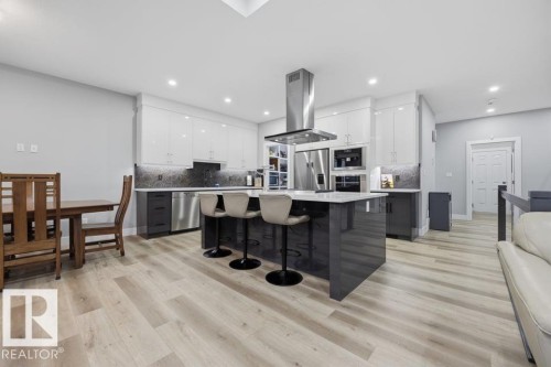 Contemporary kitchen featuring white upper cabinetry, dark lower cabinetry, stainless steel appliances, a center island with seating, and wood-finish flooring - 3303 Soleil Boulevard, Beaumont, AB - Indoor