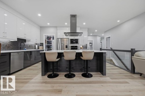 Kitchen featuring a central island with countertop seating, integrated stainless steel appliances, upper white cabinetry, lower gray cabinetry, and light wood-finish flooring - 3303 Soleil Boulevard, Beaumont, AB - Indoor Photo Showing Kitchen With Upgraded Kitchen