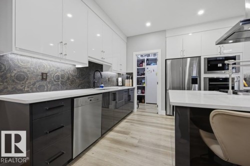 Kitchen featuring white upper cabinetry, dark lower cabinetry, patterned backsplash, light-toned wood-finish flooring, and built-in stainless steel appliances - 3303 Soleil Boulevard, Beaumont, AB - Indoor Photo Showing Kitchen With Upgraded Kitchen