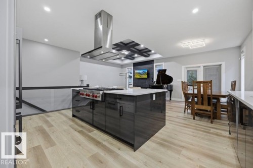 Modern kitchen island with a built-in range and stainless steel hood, set on wood-finish flooring - 3303 Soleil Boulevard, Beaumont, AB - Indoor