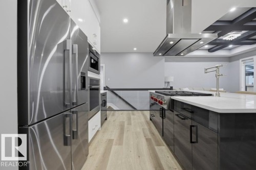 Stainless steel appliances, wood-finish flooring, white countertop, dark cabinetry, and a ceiling-mounted range hood - 3303 Soleil Boulevard, Beaumont, AB - Indoor Photo Showing Kitchen