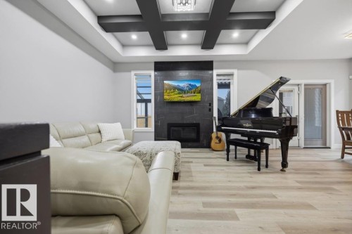 Tray ceiling with recessed lighting, integrated fireplace with dark tile surround, light wood-finish flooring, white walls, and dual pane glass doors - 3303 Soleil Boulevard, Beaumont, AB - Indoor With Fireplace