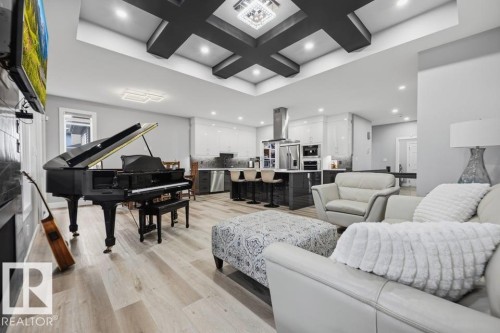 Spacious open-concept living area featuring wood-finish flooring, a tray ceiling with recessed lighting, and a modern kitchen with stainless steel appliances and an island with bar seating - 3303 Soleil Boulevard, Beaumont, AB - Indoor Photo Showing Living Room