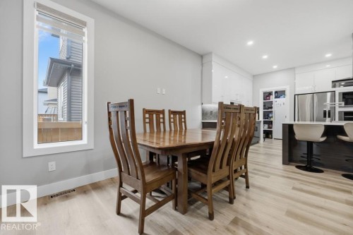 Bright dining area showcasing a wood-finish table with coordinating chairs, abundant natural light from large windows, and seamless integration with the open-concept kitchen and living spaces - 3303 Soleil Boulevard, Beaumont, AB - Indoor Photo Showing Dining Room