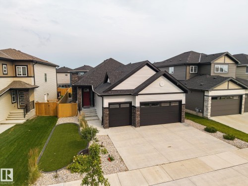 Modern exterior featuring a prominent two-car garage, stone and siding facade, and a red entry door - 3303 Soleil Boulevard, Beaumont, AB - Outdoor With Facade