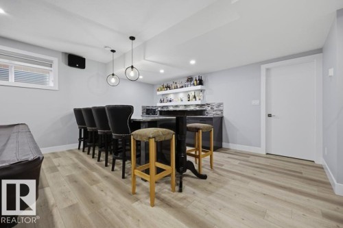 Recessed and pendant lighting illuminate the wood-finish flooring, complemented by a built-in bar with a tiled backsplash and floating shelves - 3303 Soleil Boulevard, Beaumont, AB - Indoor