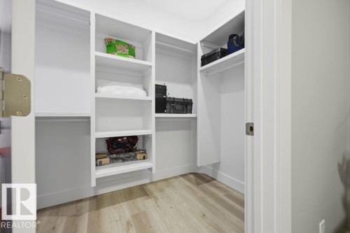 Integrated white shelving system with hanging rods and wood-finish flooring - 3303 Soleil Boulevard, Beaumont, AB - Indoor With Storage