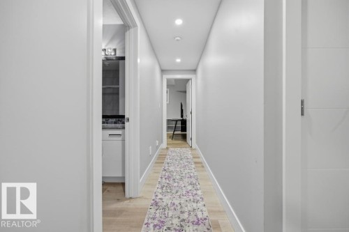 Modern hallway with recessed ceiling lights, clean white walls, wood-finish flooring, and a decorative runner rug leading toward additional living spaces - 3303 Soleil Boulevard, Beaumont, AB - Indoor Photo Showing Other Room