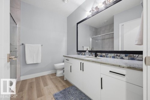 Spacious bathroom featuring a white vanity with dark hardware, stone-finish countertop, undermount sink, and wood-finish flooring - 3303 Soleil Boulevard, Beaumont, AB - Indoor Photo Showing Bathroom