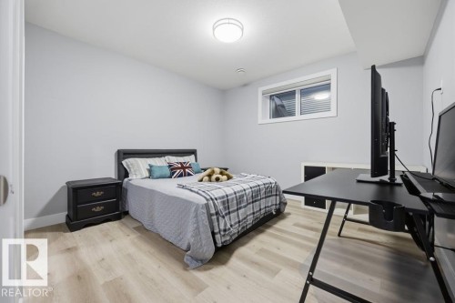 Versatile bedroom featuring wood-finish flooring, a black bed frame with upholstered headboard, black nightstand with drawer storage, and a dedicated workspace with black desk and dual monitor setup - 3303 Soleil Boulevard, Beaumont, AB - Indoor Photo Showing Bedroom