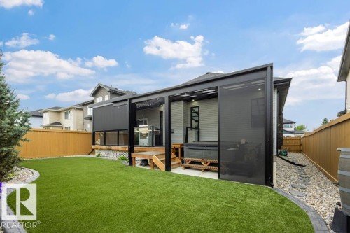 Modern backyard retreat featuring a manicured lawn, contemporary covered patio with sliding glass doors, composite decking with wood-finish detailing, gravel landscaping borders, and wooden privacy fencing - 3303 Soleil Boulevard, Beaumont, AB - Outdoor With Deck Patio Veranda