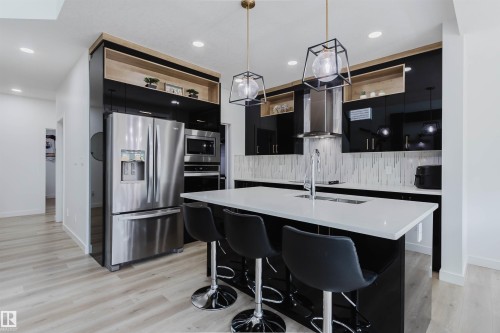 Kitchen featuring light wood-finish flooring, a white countertop island with integrated sink, black high-gloss cabinetry, and stainless steel appliances - 5320 Kimball Place Sw, Edmonton, AB - Indoor Photo Showing Kitchen With Upgraded Kitchen