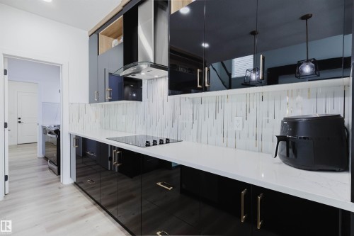 Sleek kitchen featuring black high-gloss cabinetry, white countertop, linear tile backsplash, and a built-in electric cooktop - 5320 Kimball Place Sw, Edmonton, AB - Indoor Photo Showing Kitchen