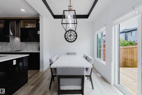 Open-concept dining area with wood-finish flooring, featuring a modern chandelier, and a sliding glass door leading to a wood deck - 5320 Kimball Place Sw, Edmonton, AB - Indoor Photo Showing Dining Room