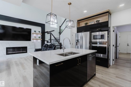 Kitchen island with an undermount dual-basin sink, stainless steel appliances, and wood-finish flooring - 5320 Kimball Place Sw, Edmonton, AB - Indoor Photo Showing Kitchen With Fireplace With Double Sink With Upgraded Kitchen