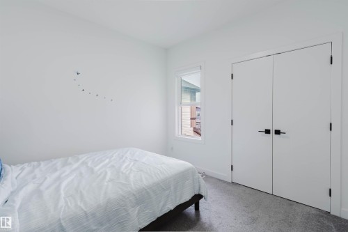 White walls, carpet flooring, window with white trim, and a white bi-fold closet door with black hardware - 5320 Kimball Place Sw, Edmonton, AB - Indoor Photo Showing Bedroom