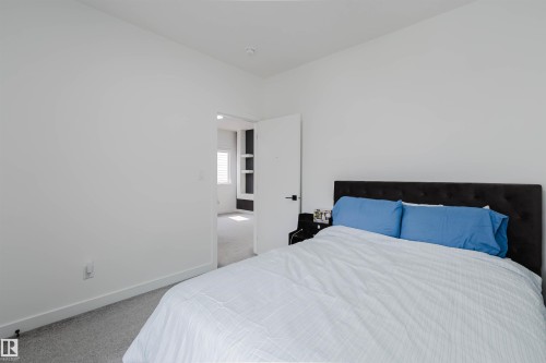 Bright bedroom featuring neutral walls, carpeted flooring, and a black upholstered bed frame with blue accent pillows - 5320 Kimball Place Sw, Edmonton, AB - Indoor Photo Showing Bedroom