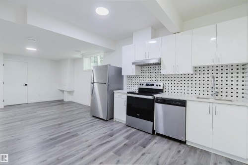 Galley kitchen featuring white cabinetry, stainless steel appliances, a square tile backsplash, and light wood-finish flooring - 5320 Kimball Place Sw, Edmonton, AB - Indoor Photo Showing Kitchen