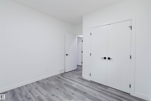 Light-toned wood-finish flooring, white walls, white doors with black hardware, and white trim - 5320 Kimball Place Sw, Edmonton, AB - Indoor Photo Showing Other Room