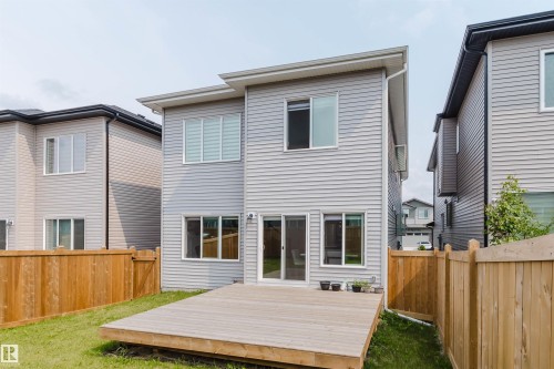 Rear exterior featuring light gray siding, a wood deck, sliding glass doors, multiple windows, and a wood privacy fence - 5320 Kimball Place Sw, Edmonton, AB - Outdoor With Exterior