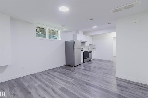 Open concept living area featuring wood-finish flooring, recessed lighting, and a kitchen with stainless steel appliances, white cabinetry, and a tile backsplash - 5320 Kimball Place Sw, Edmonton, AB - Indoor Photo Showing Kitchen