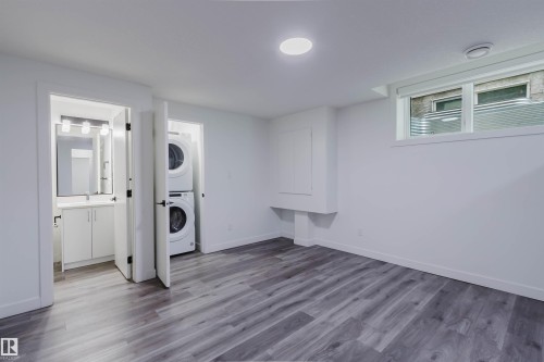 Recessed ceiling lighting, wood-finish flooring, built-in stacked laundry appliances, white vanity with integrated sink, and horizontal window - 5320 Kimball Place Sw, Edmonton, AB - Indoor Photo Showing Laundry Room