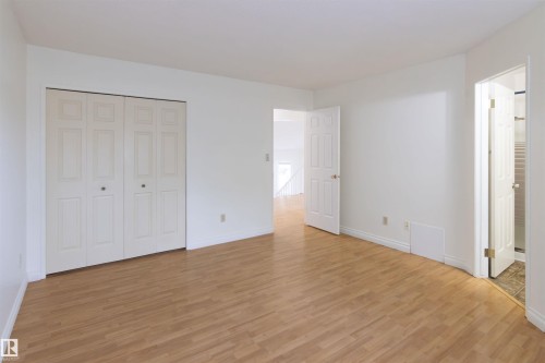 Spacious bedroom featuring wood-finish flooring, multiple closet storage options with bi-fold doors, and abundant natural light from multiple windows - 4903 11A Avenue Nw, Edmonton, AB - Indoor