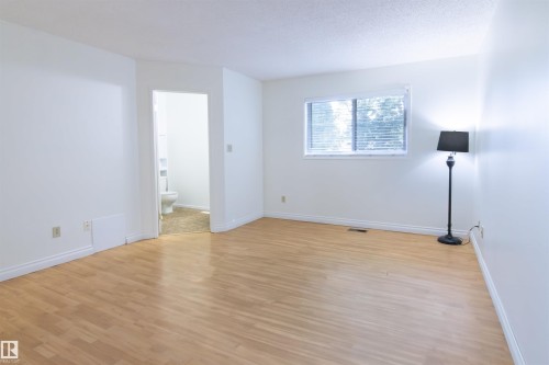 Bright interior space featuring wood-finish flooring, white baseboards, and a window with blinds - 4903 11A Avenue Nw, Edmonton, AB - Indoor Photo Showing Other Room