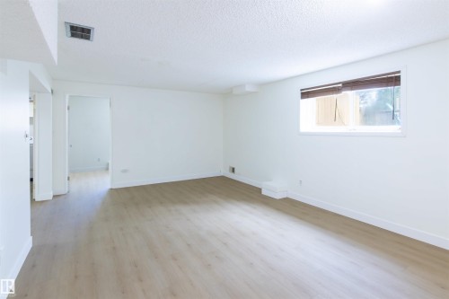 Expansive room featuring wood-finish flooring, white baseboards, and a window with blinds - 4903 11A Avenue Nw, Edmonton, AB - Indoor Photo Showing Other Room