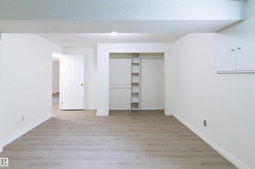 Spacious room featuring light wood-finish flooring, white baseboards, and a built-in closet with shelving and hanging rods - 4903 11A Avenue Nw, Edmonton, AB - Indoor Photo Showing Other Room