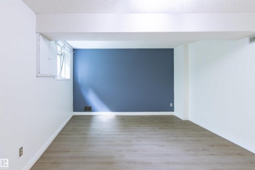Open room featuring wood-finish flooring, white walls with an accent wall in a deep blue hue, and a textured ceiling - 4903 11A Avenue Nw, Edmonton, AB - Indoor Photo Showing Other Room