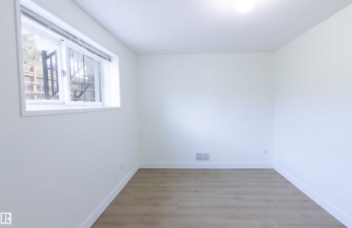 Bright room featuring a large window, light wood-finish flooring, white walls, white baseboards, and a ceiling-mounted light fixture - 4903 11A Avenue Nw, Edmonton, AB - Indoor Photo Showing Other Room