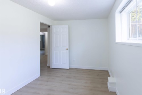 Bright and airy bedroom featuring wood-finish flooring, abundant natural light from a large window, and seamless access to adjoining spaces through a six-panel interior door - 4903 11A Avenue Nw, Edmonton, AB - Indoor Photo Showing Other Room