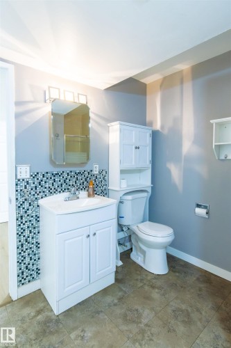 Bathroom featuring a white corner vanity with an integrated sink, mosaic tile backsplash, and a wall-mounted medicine cabinet with a four-bulb vanity light including laundry room - 4903 11A Avenue Nw, Edmonton, AB - Indoor Photo Showing Bathroom