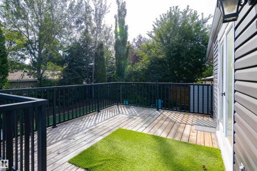 Expansive composite deck featuring a wood-finish surface and black metal railing system, overlooking a manicured lawn with mature landscaping - 4903 11A Avenue Nw, Edmonton, AB - Outdoor