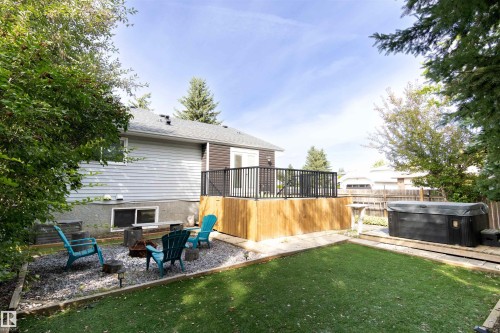 Expansive backyard featuring a manicured lawn, a gravel fire pit area, a multi-level wood deck with black metal railing, and a hot tub on a wooden platform - 4903 11A Avenue Nw, Edmonton, AB - Outdoor With Deck Patio Veranda
