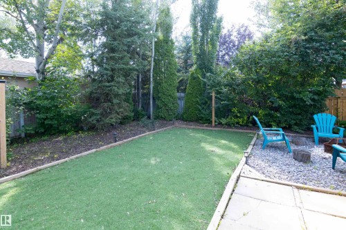 Expansive backyard featuring artificial turf, a gravel seating area, mature trees, and a wooden fence - 4903 11A Avenue Nw, Edmonton, AB - Outdoor