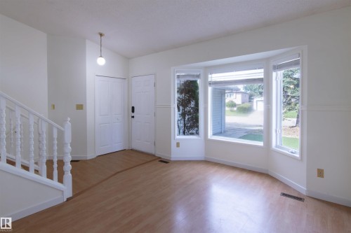 Spacious living area featuring wood-finish flooring, a prominent bay window, and a white painted staircase with spindle railing - 4903 11A Avenue Nw, Edmonton, AB - Indoor Photo Showing Other Room