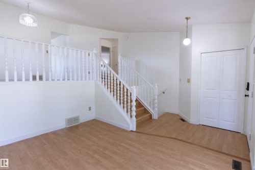 Split-level living room featuring wood-finish flooring, white spindle railings, and a bi-fold closet door - 4903 11A Avenue Nw, Edmonton, AB - Indoor Photo Showing Other Room