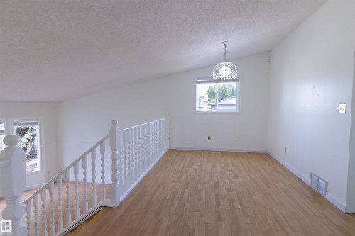 Spacious upper-level dining room featuring wood-finish flooring, abundant natural light from a transom window, and a railed mezzanine overlooking the lower level - 4903 11A Avenue Nw, Edmonton, AB - Indoor Photo Showing Other Room